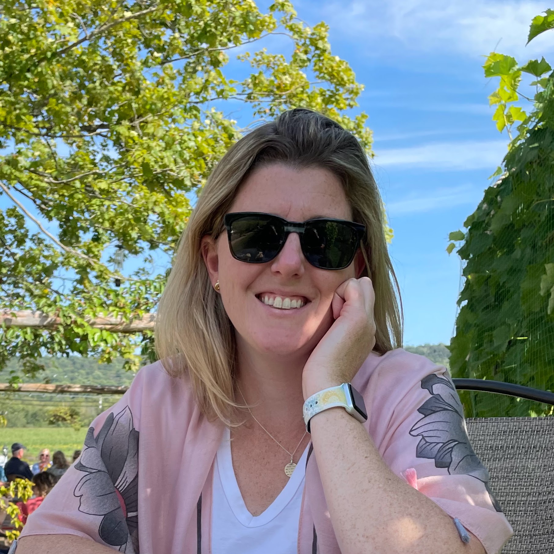 image of Nicole with sunglasses smiling at camera with trees and vines in background